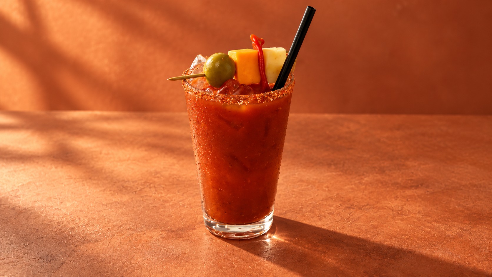 Red garnished cocktail styled against a warm terracotta background