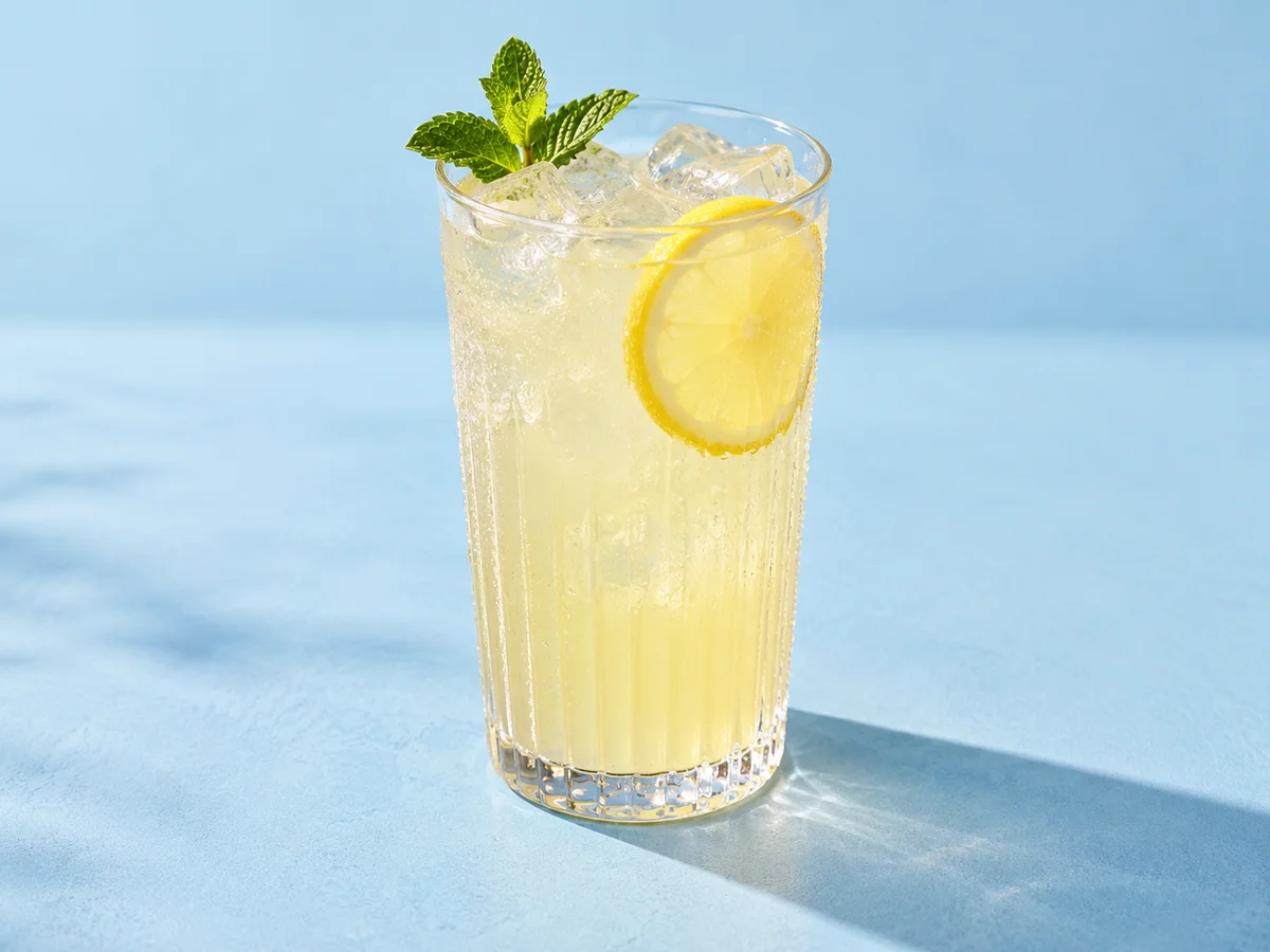 Cloudy lemonade with ice, a lemon slice and mint in a ribbed glass on a pale blue surface
